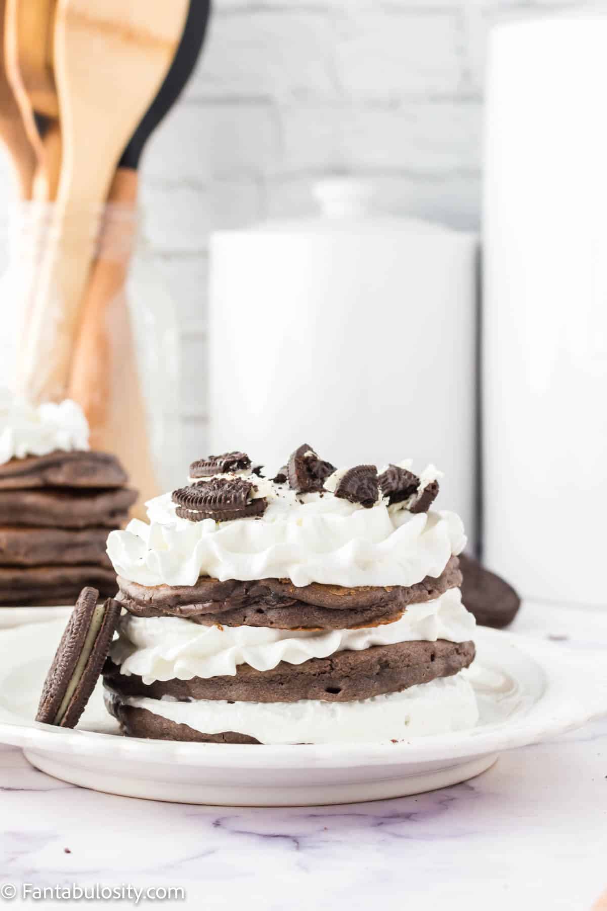 Oreo pancakes, stacked on white plate with whipped cream.