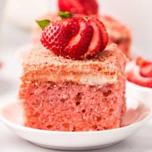 Slice of strawberry cake on white plate with fresh strawberries on top.