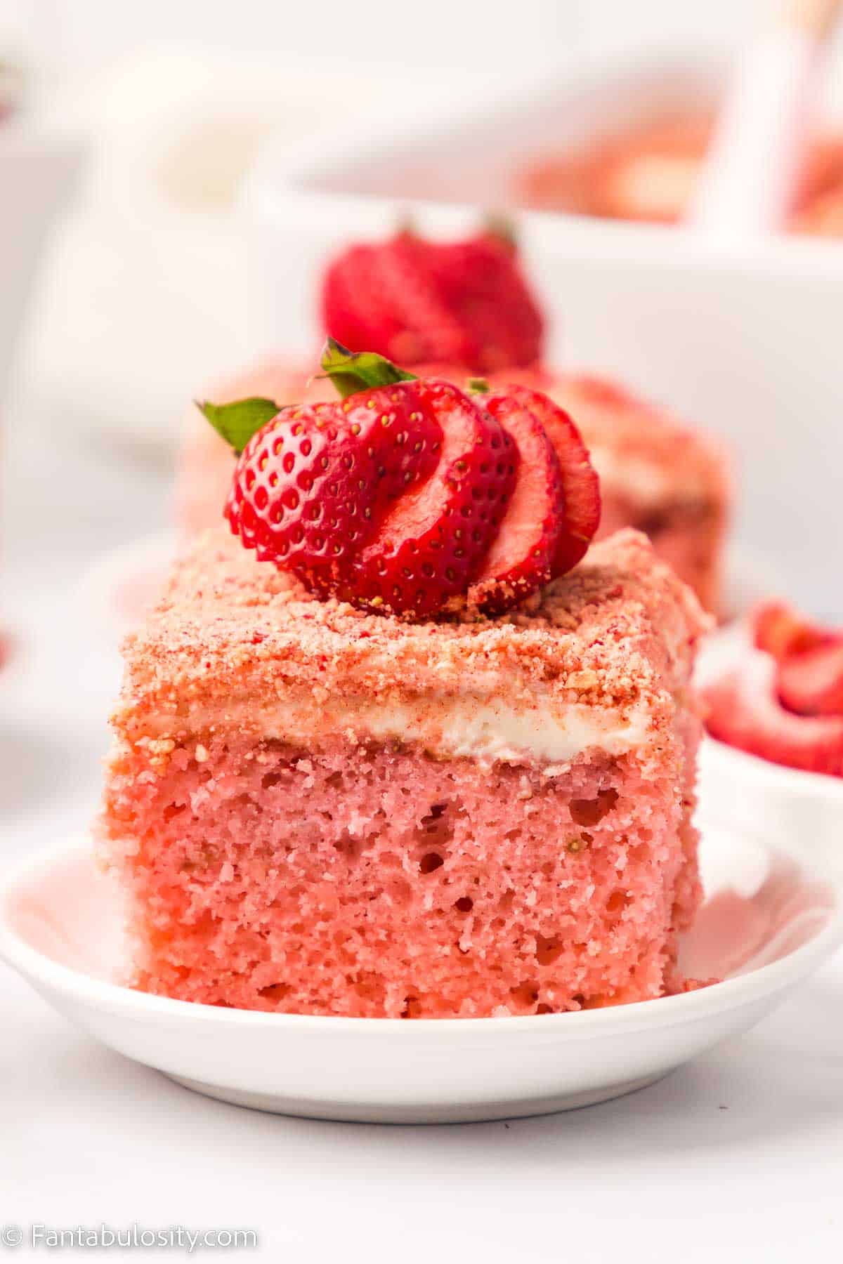 Slice of strawberry crunch cake on white plate, with fresh strawberries on top.