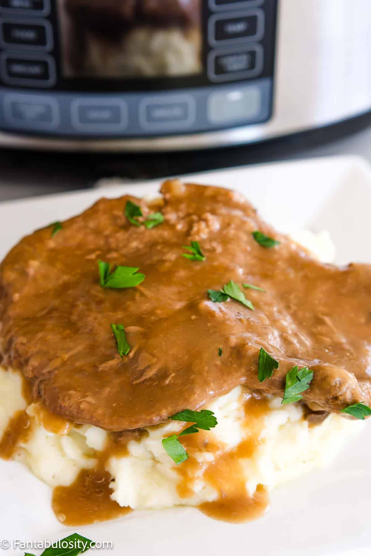 Crock Pot cube steak on top of mashed potatoes, sitting in front of slow cooker.