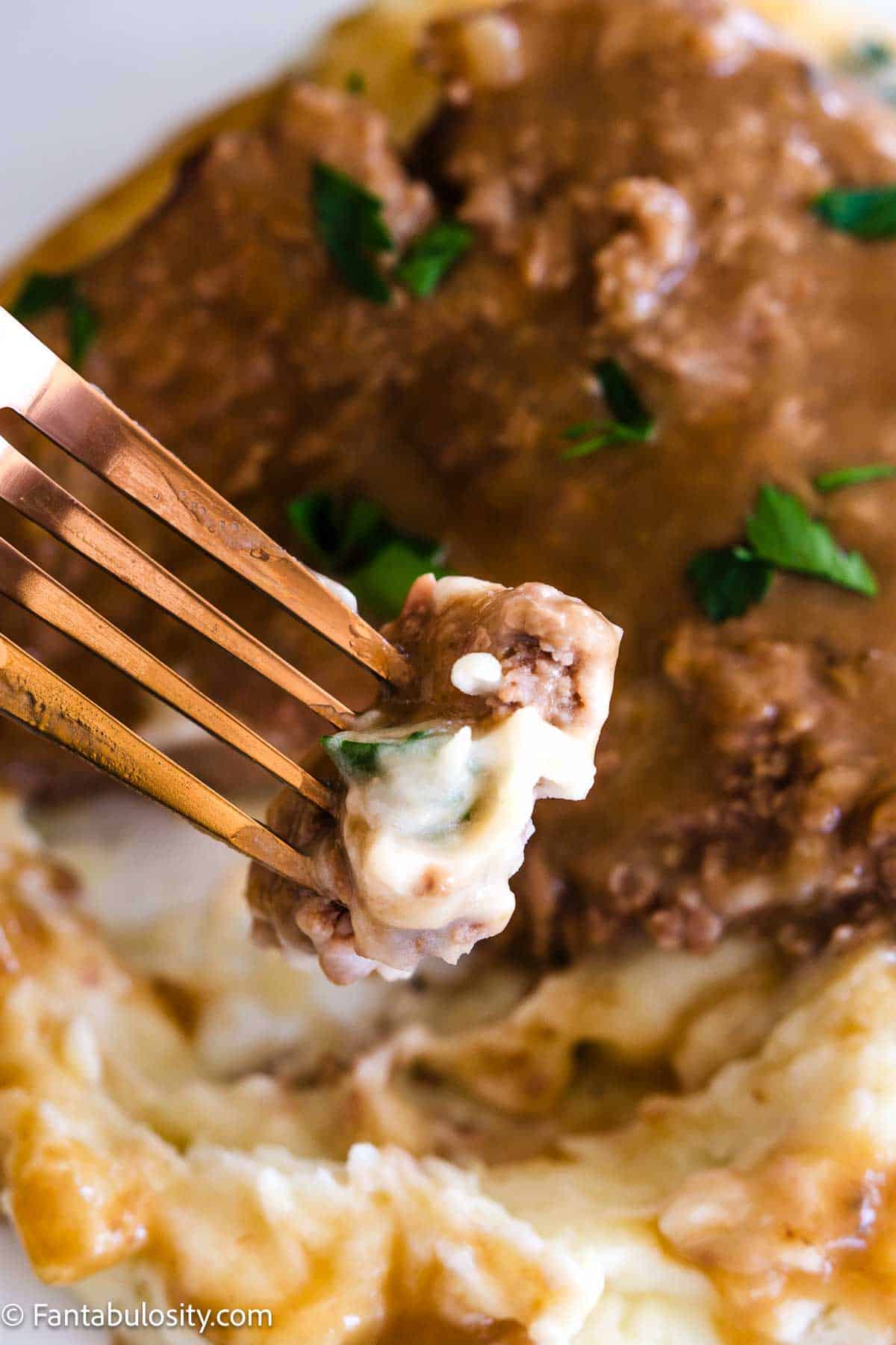 Bite of Crock Pot cube steak on fork, above plate of mashed potatoes.