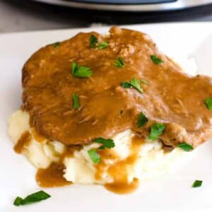 Crock Pot cube steak on top of mashed potatoes, sitting on white plate.