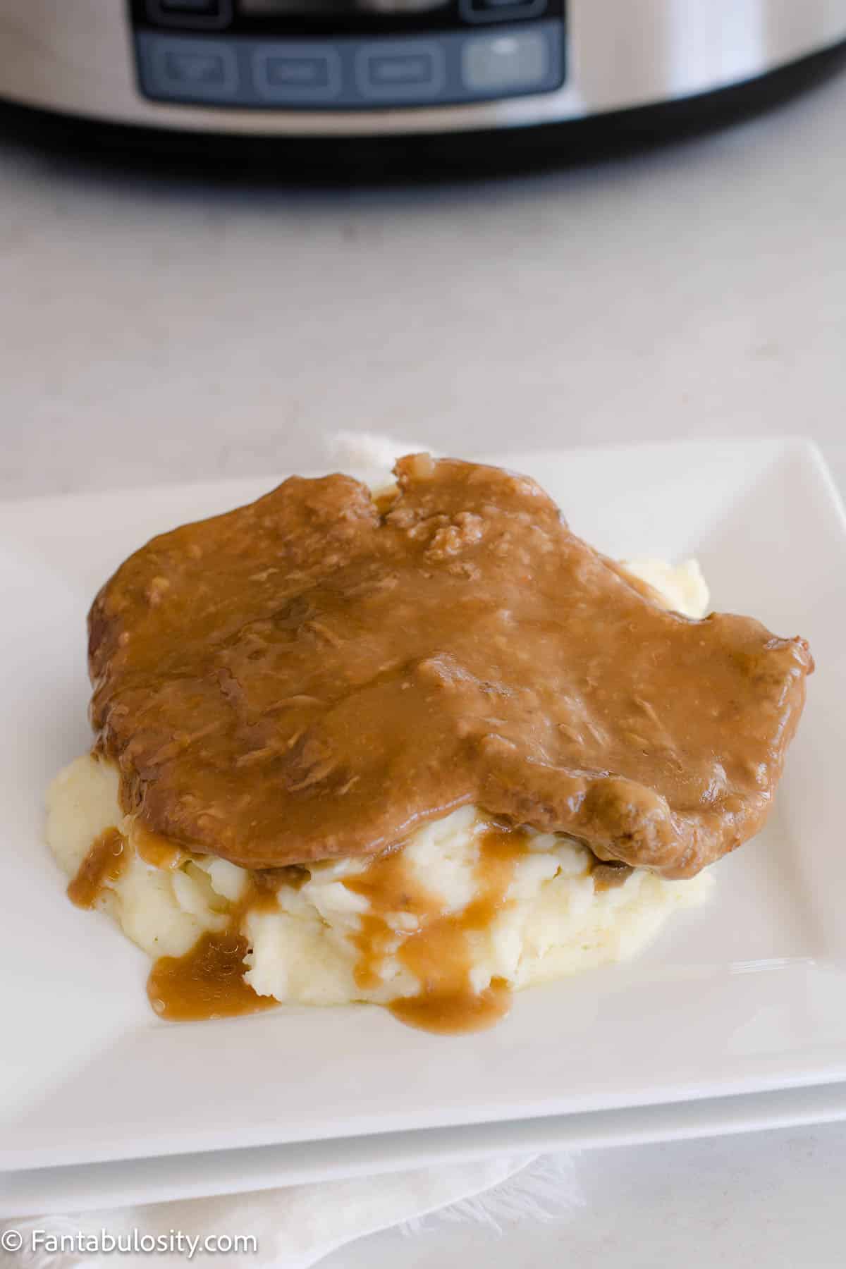 Slow cooked cubed steak on top of mashed potatoes, on white plate.