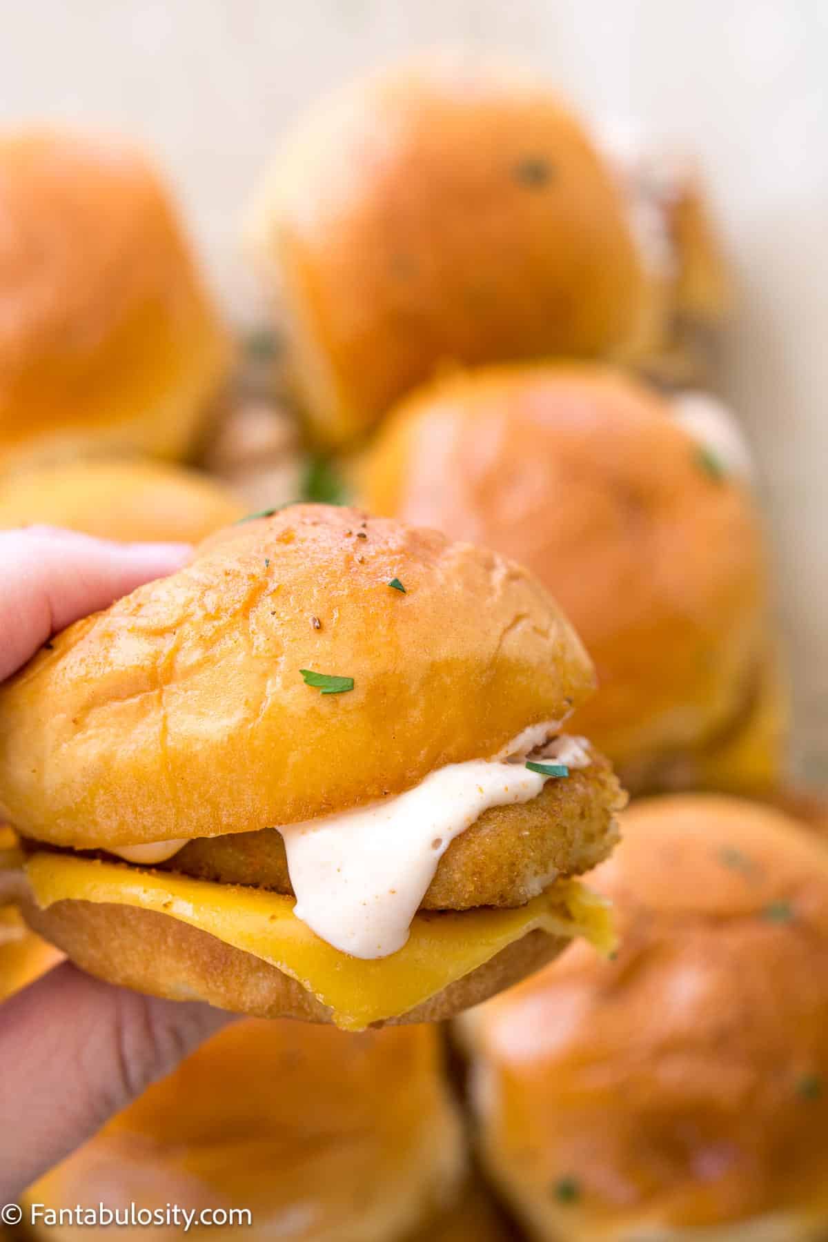 Hand holding fish slider with Old Bay sauce drizzled on top.