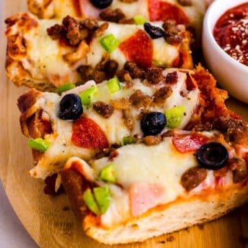 French bread pizza, sliced on wooden cutting board.