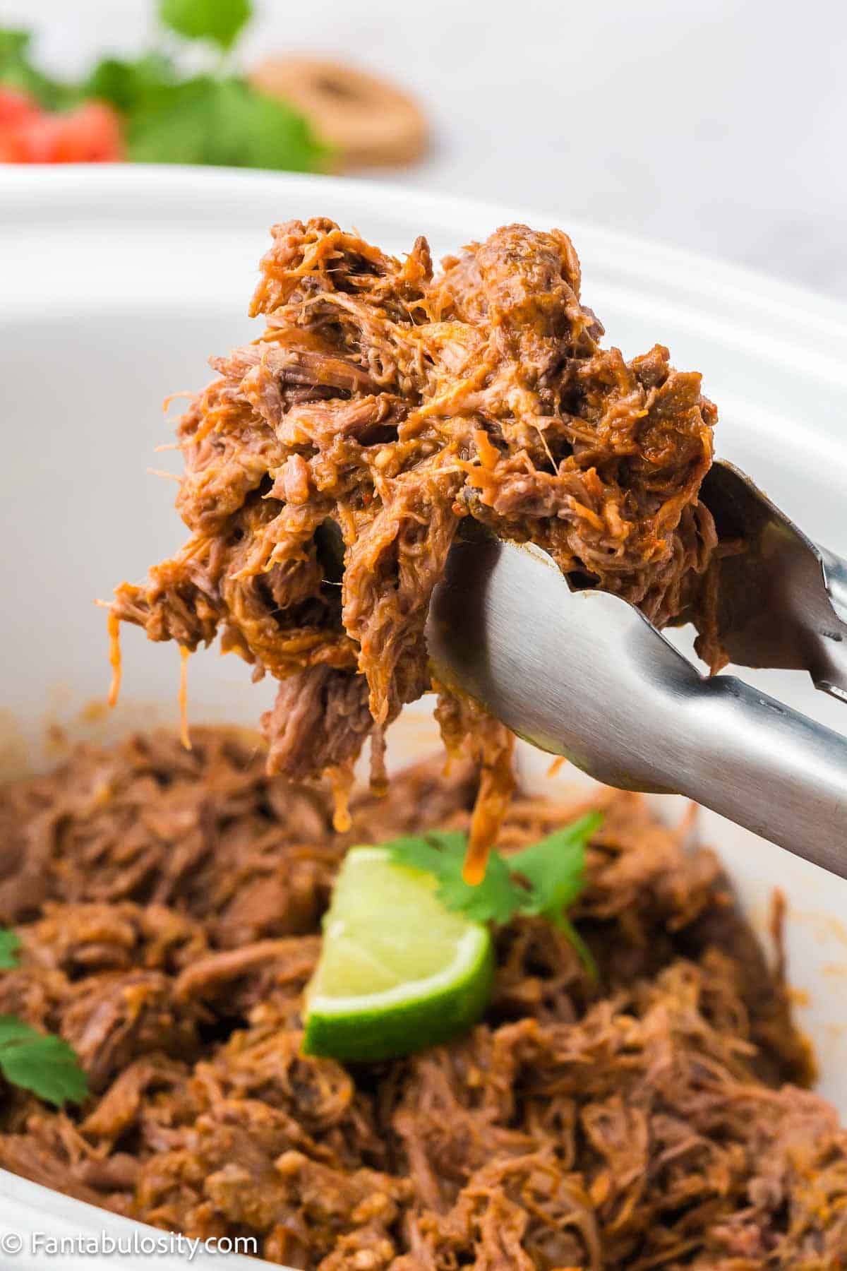 Cooked taco flavored beef lifting out of slow cooker with tongs.