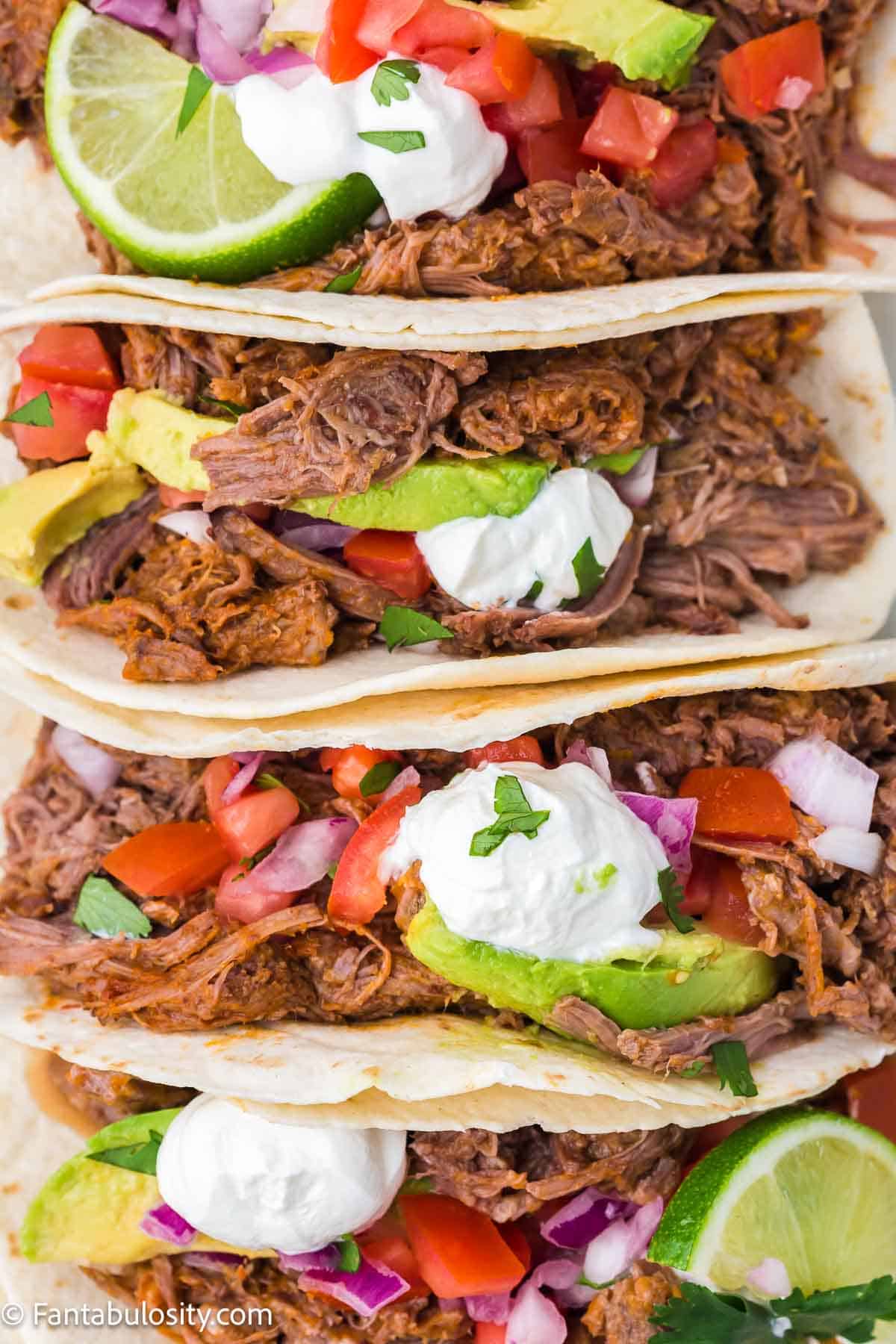 Shredded beef tacos folded up in line with toppings.