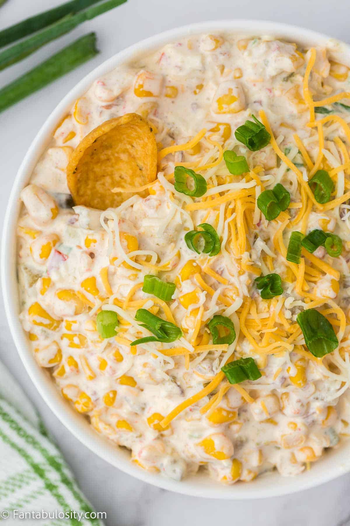 Corn dip mixed and in white bowl, with corn chip in dip.