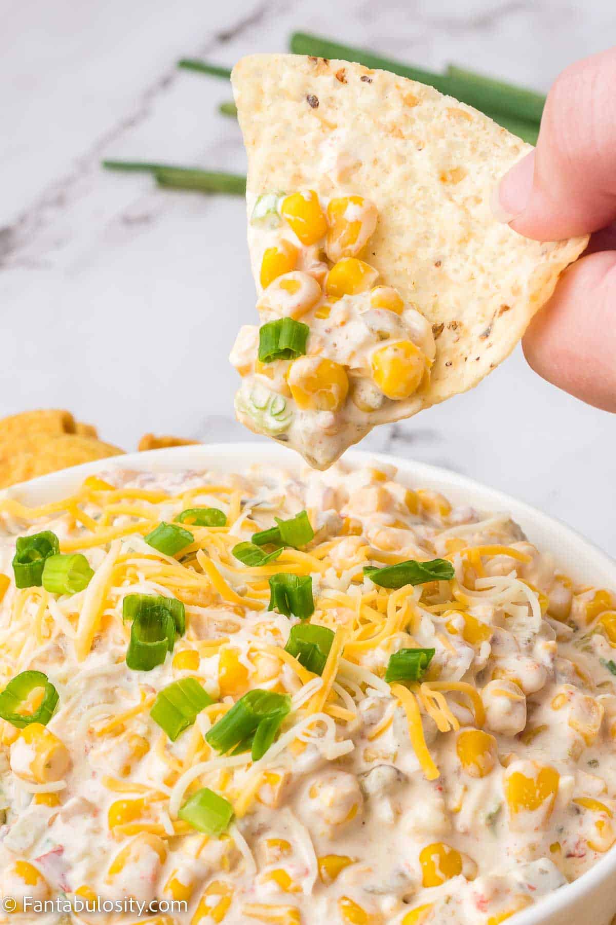 Tortilla chip dipping in to corn dip, lifting out a bite.