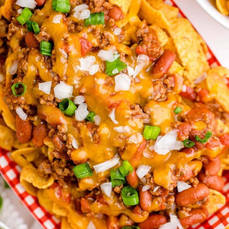 Fritos, chili, cheese, onions, all piled together in cardboard dish.