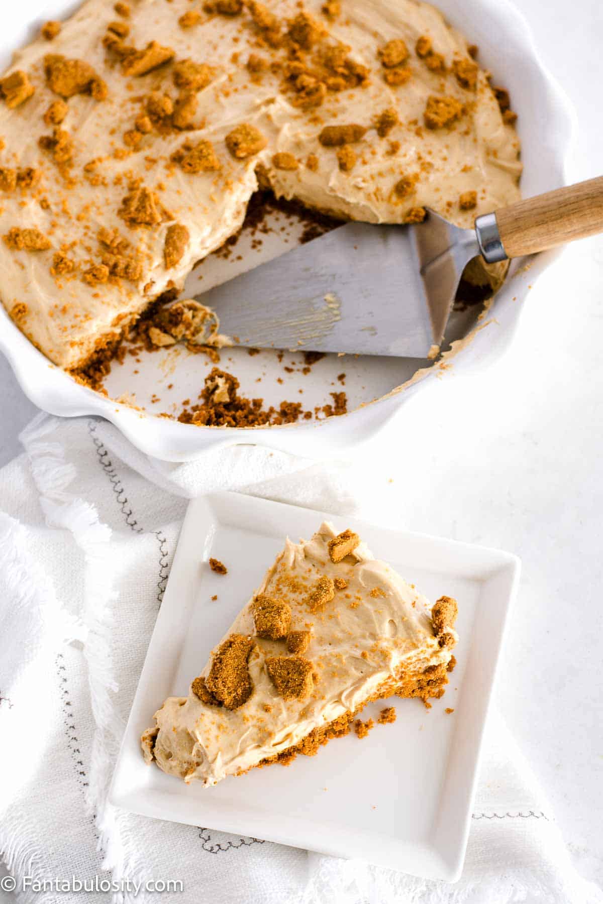 Slice of Biscoff pie on white plate, next to whole pie.