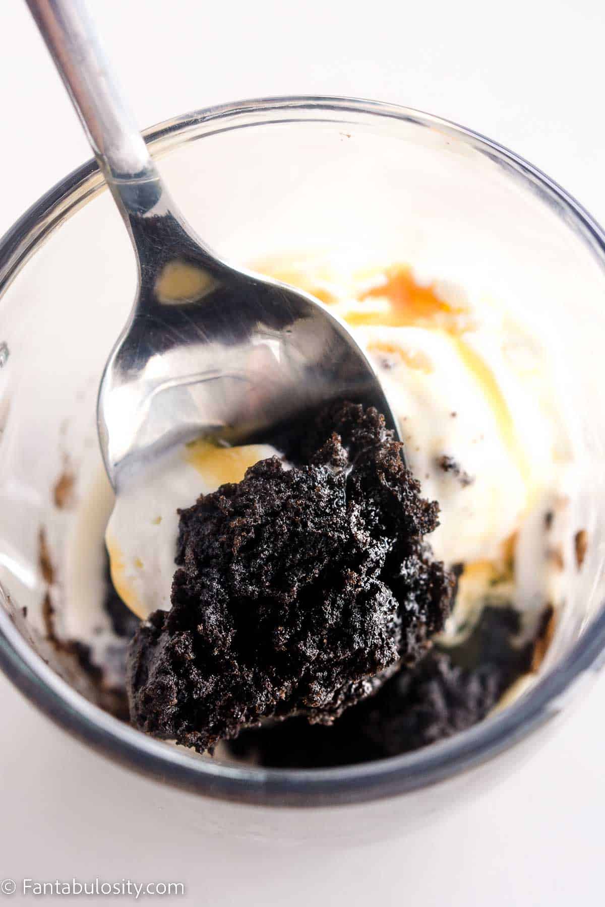 Oreo mug cake with spoon lifting out whipped cream and caramel sauce.