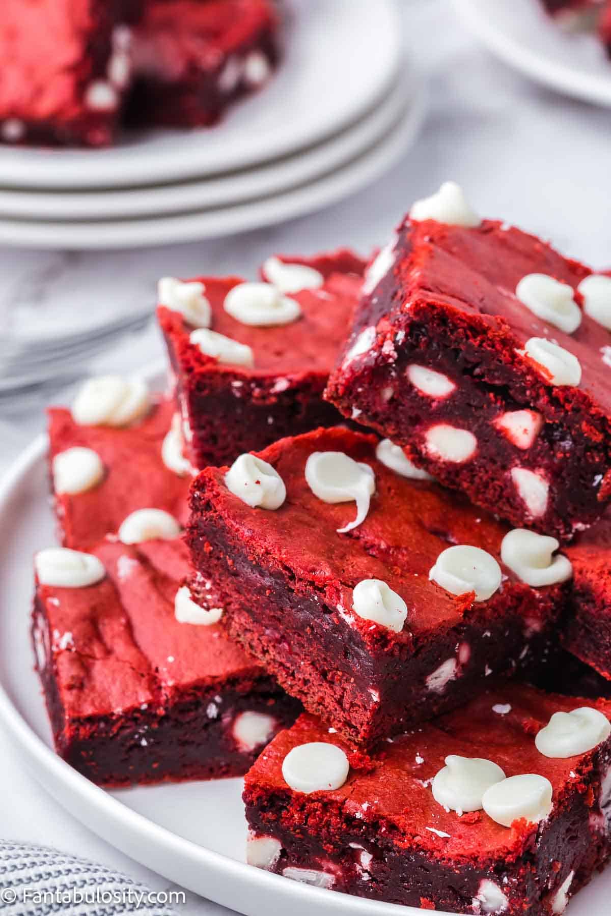 Stack of red velvet brownies on white plate.