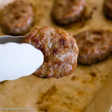Cooked sausage patty being held by tongs.
