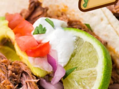 Close up of shredded beef taco on white plate, topped with taco toppings.