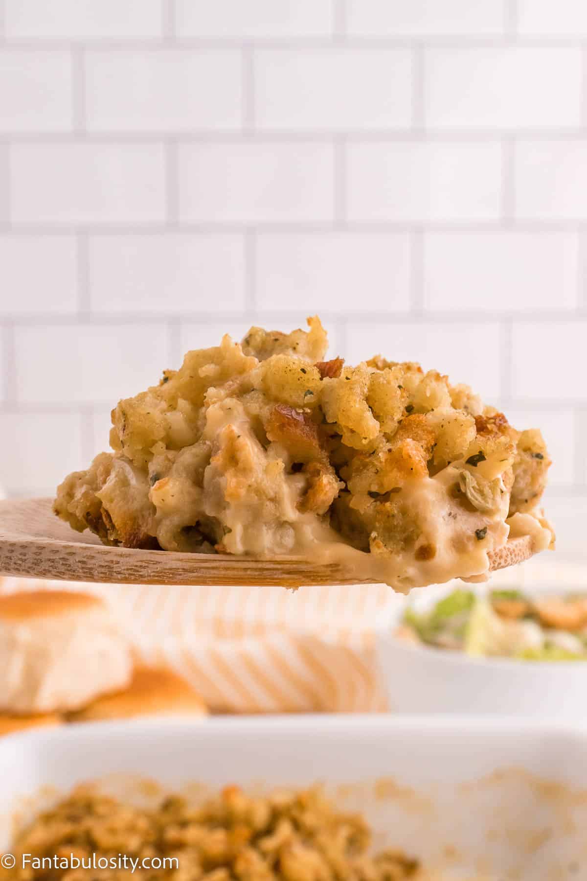 Stove Top Stuffing Chicken Casserole on wooden spatula, lifting out of casserole dish.