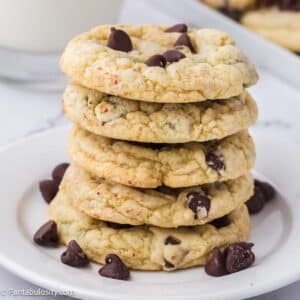 Chocolate chip sugar cookies stacked on top of one another, sitting on white plate.