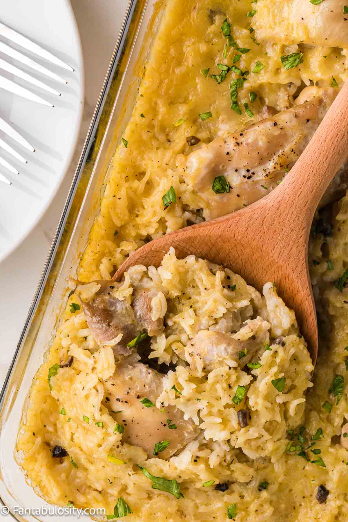 Close up of chicken and rice casserole on wooden spoon in baking dish.