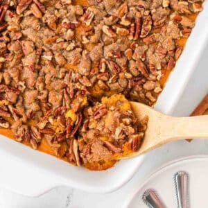 Sweet potato crunch in white baking dish, with wooden spoon dipping out.