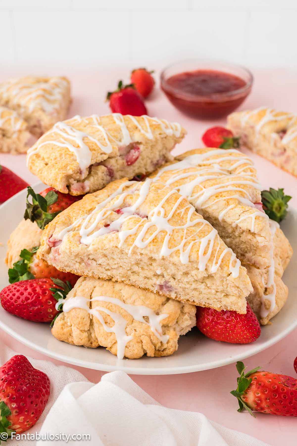 Bisquick strawberry scones sitting on white plate, surrounded by whole strawberries.