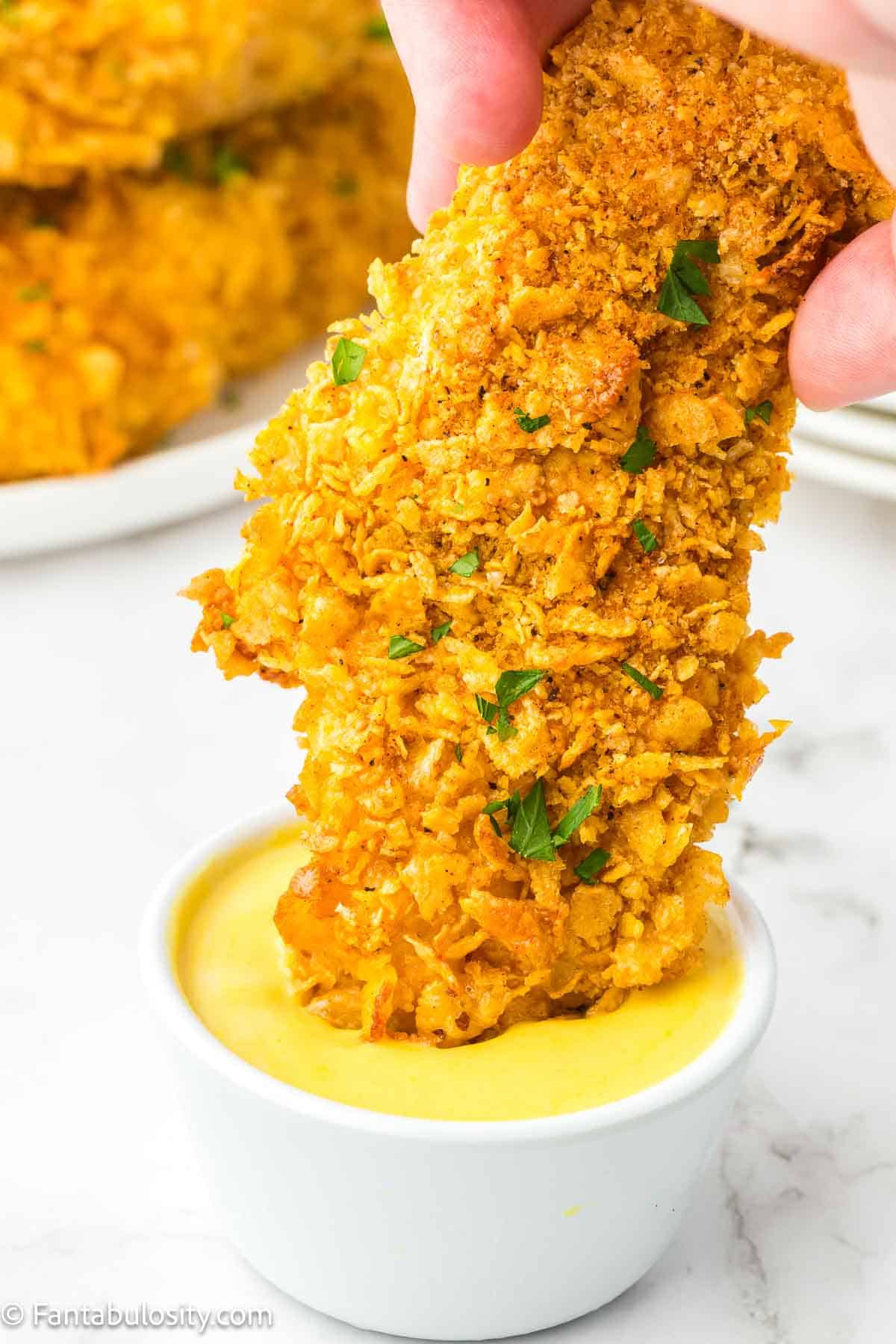 Cooked piece of cornflake chicken dipping in to mustard.
