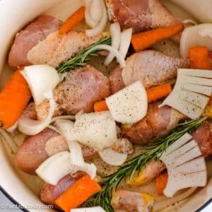 Raw chicken legs in dutch oven with veggies.