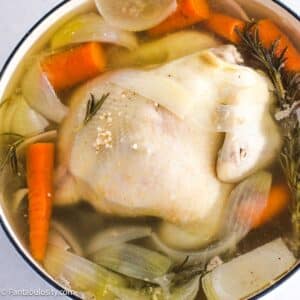 Whole chicken in dutch oven, boiling with vegetables.