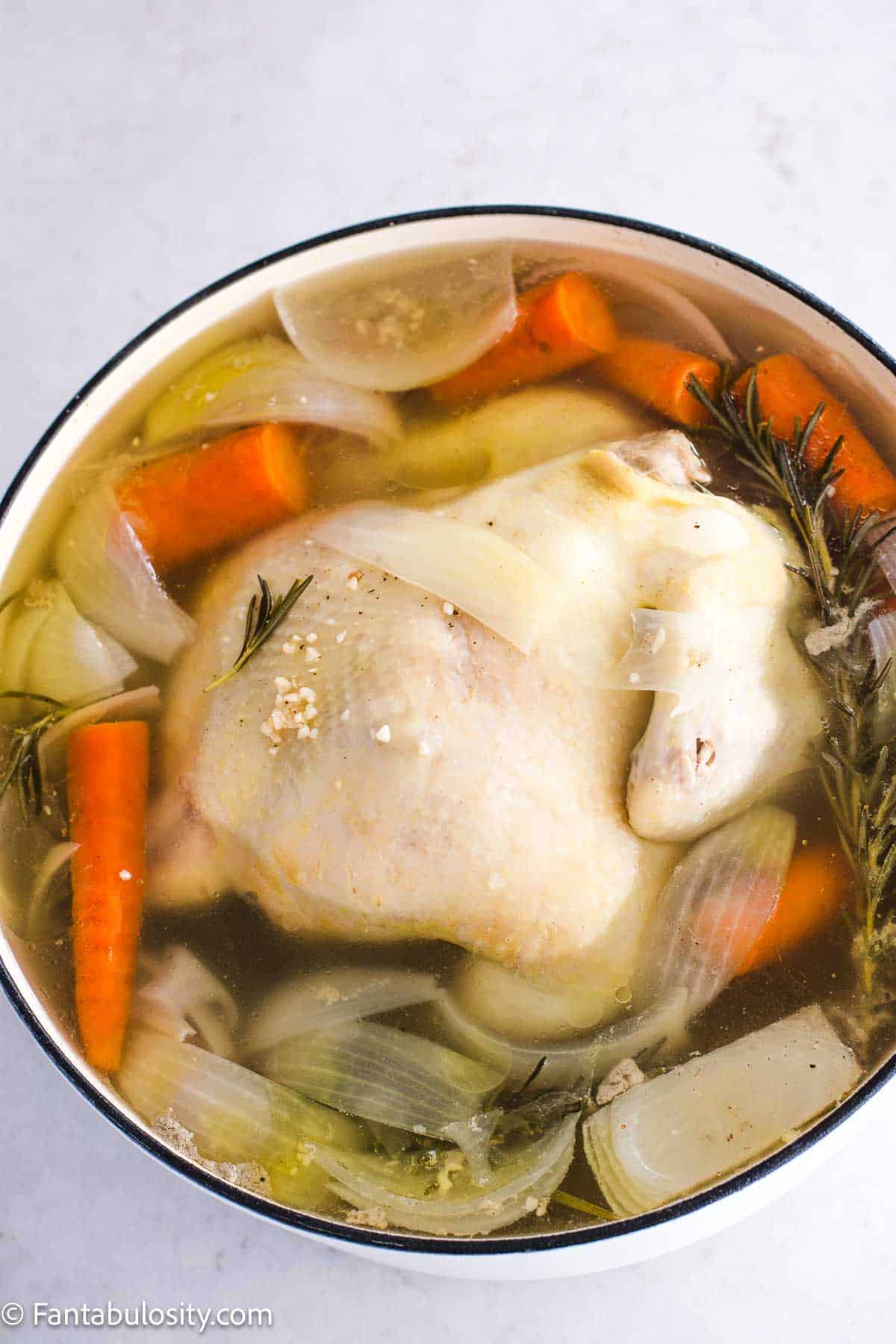 Raw, whole chicken in dutch oven, with water, vegetables and seasonings.