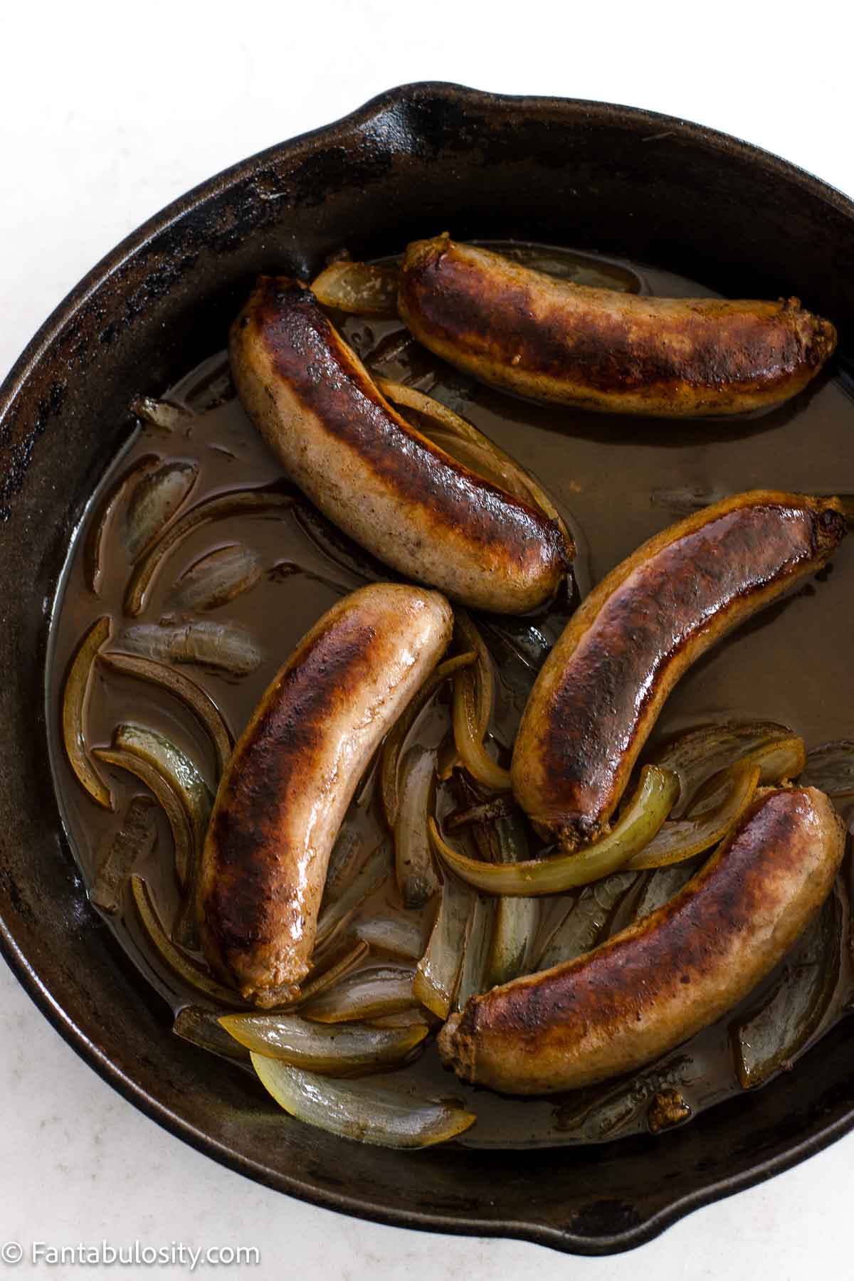 Cooked bratwursts in cast iron pan, with cooked onions.