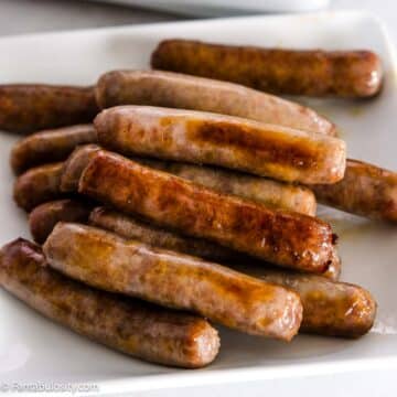Breakfast sausage links, cooked, and sitting on a white plate.