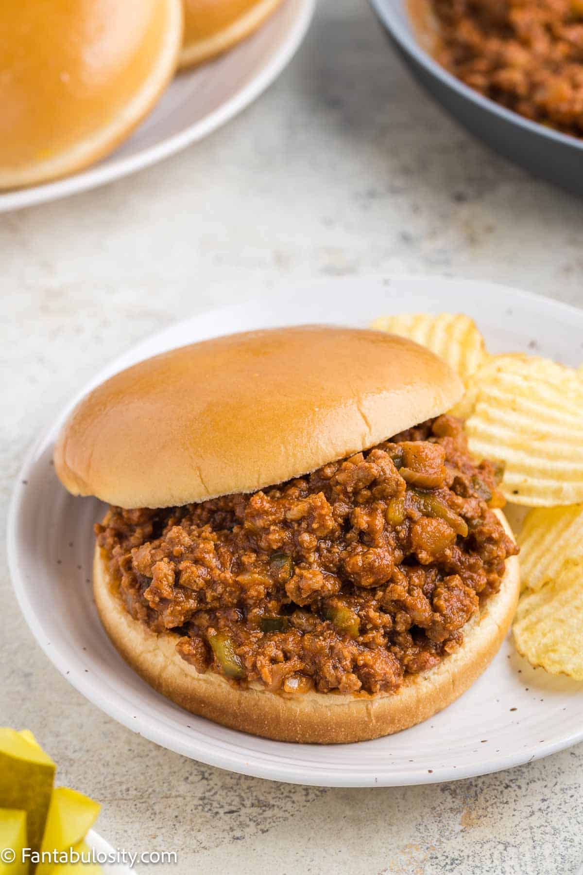 Old fashioned sloppy joe sandwich on white plate, next to potato chips.