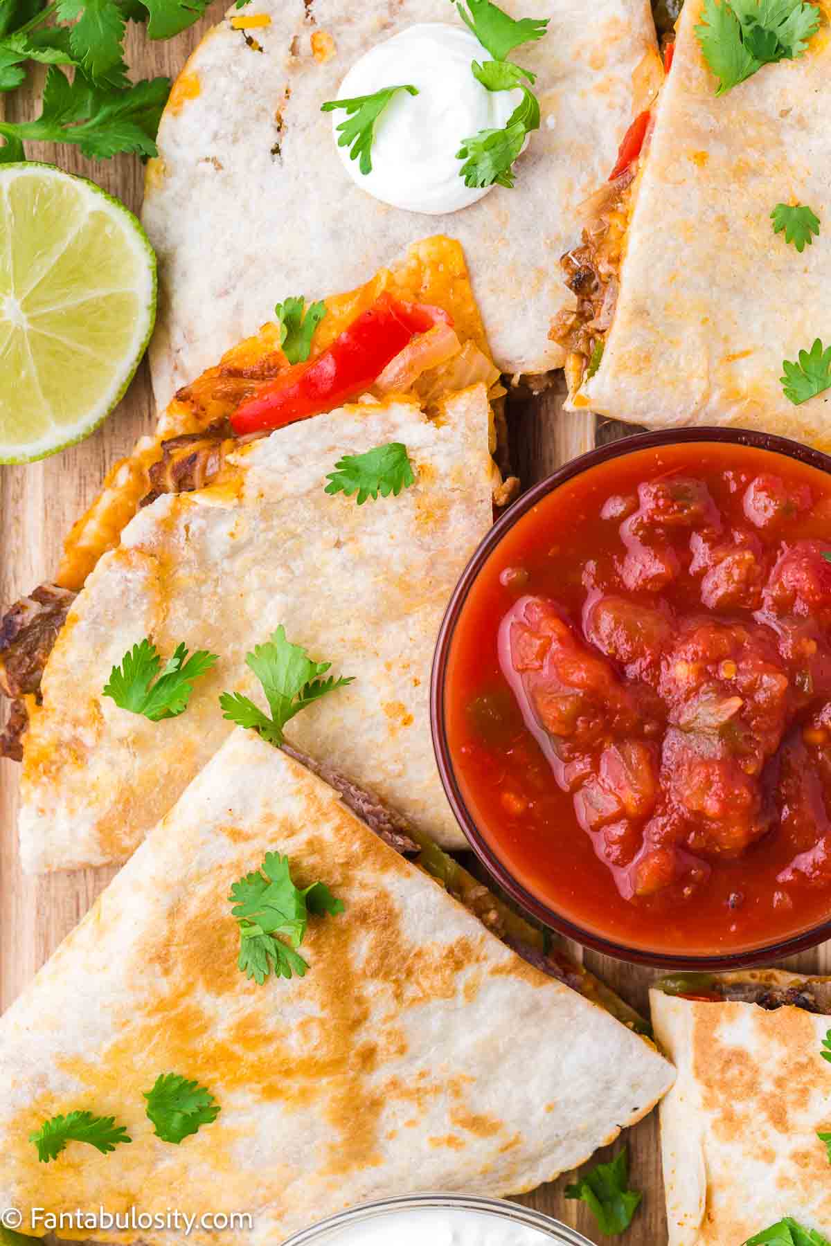 Steak quesadilla slices sitting next to salsa.