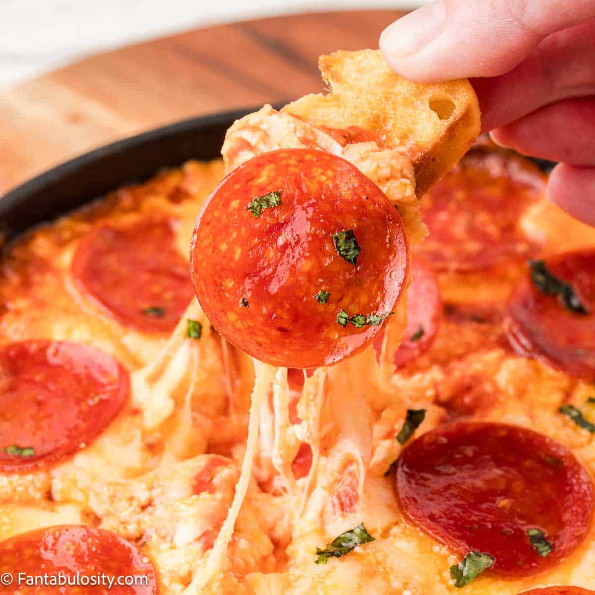 Hand dipping crostini in pepperoni dip.