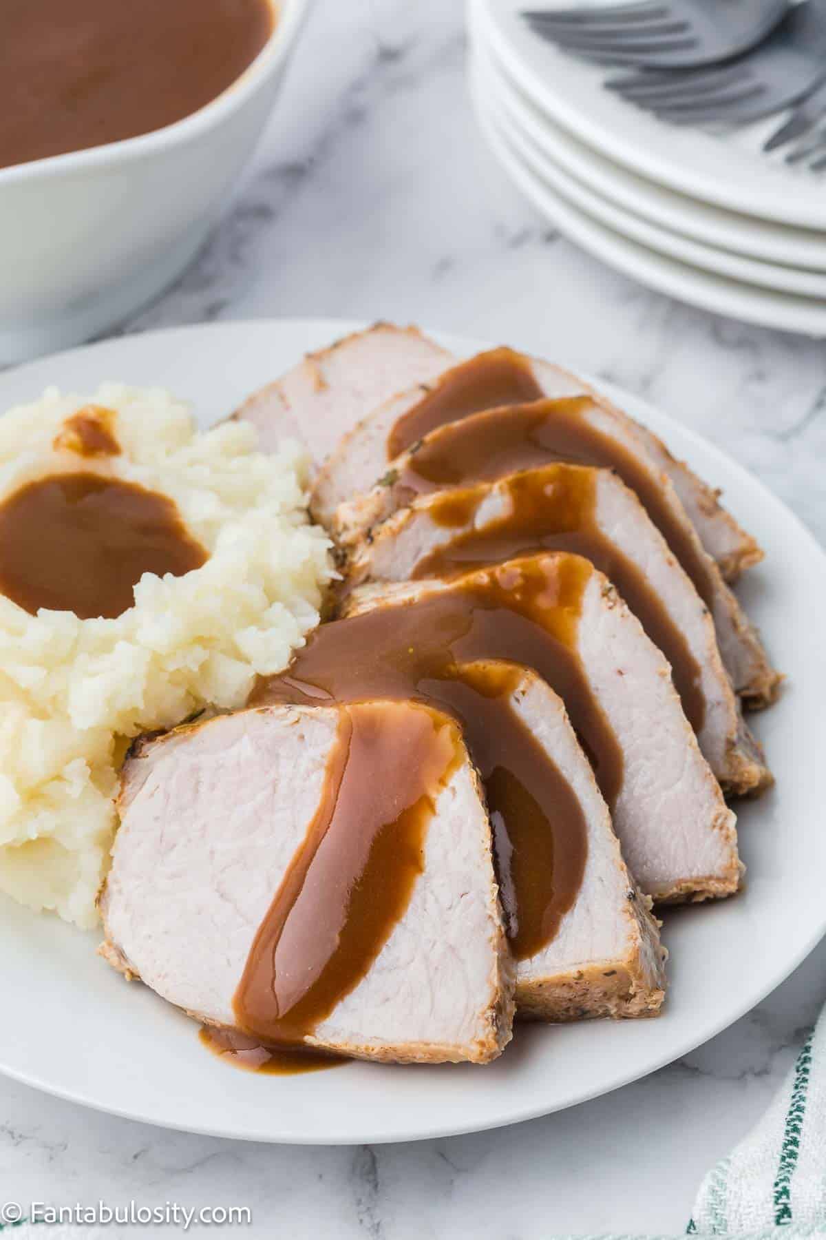 Pork gravy drizzled over cooked pork loin, sitting on white plate.