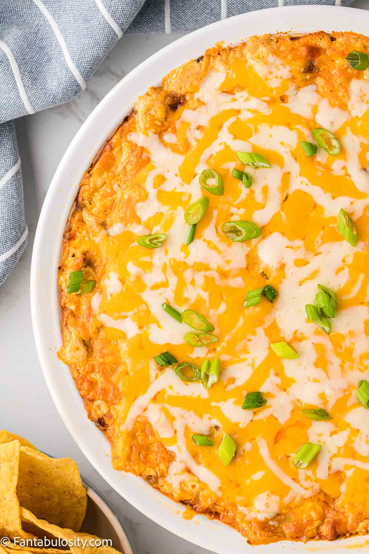 Close up of buffalo chicken dip in white pie dish, with cheese and green onions sprinkled on top.