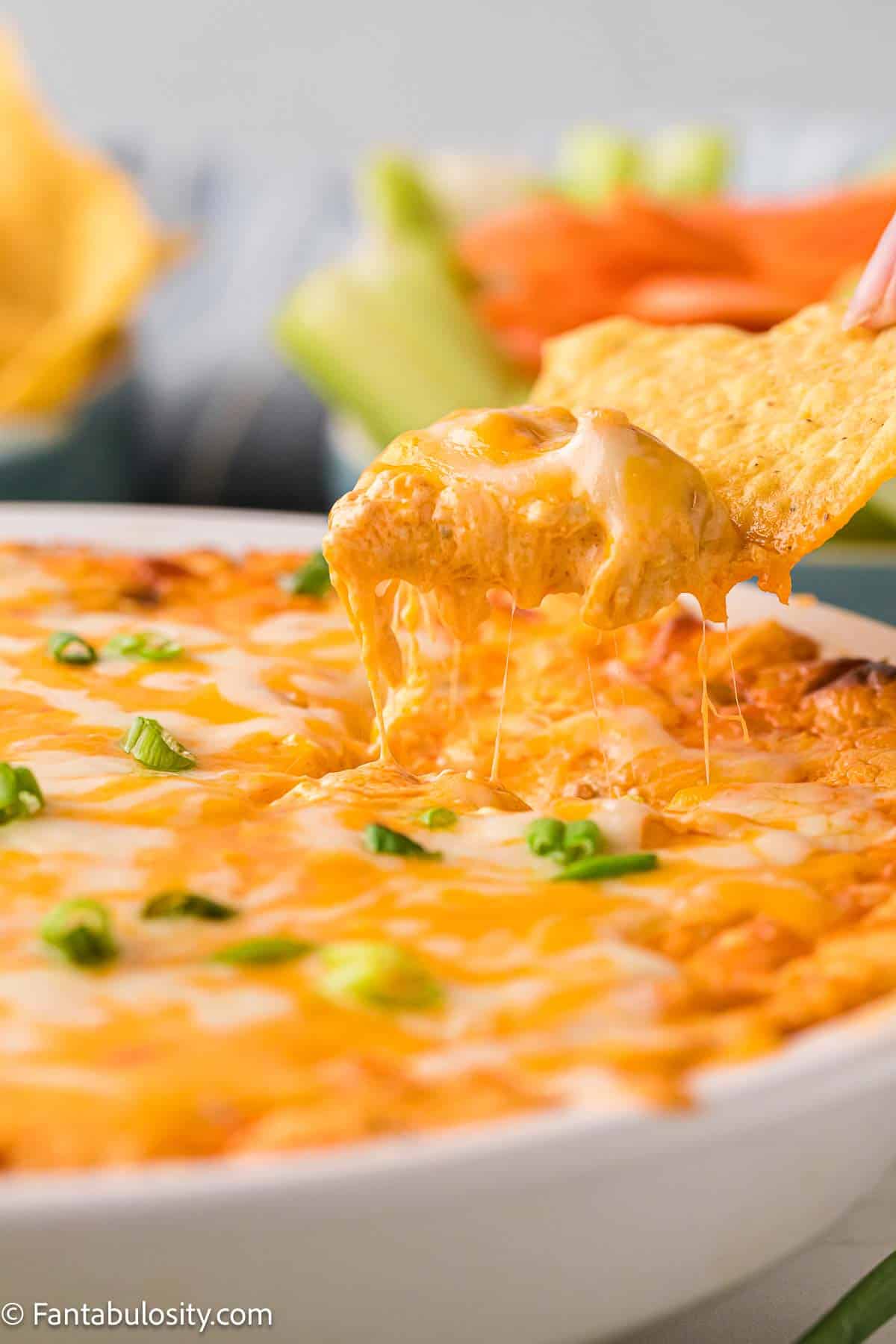 Chip pulling buffalo chicken dip up out of baking dish.