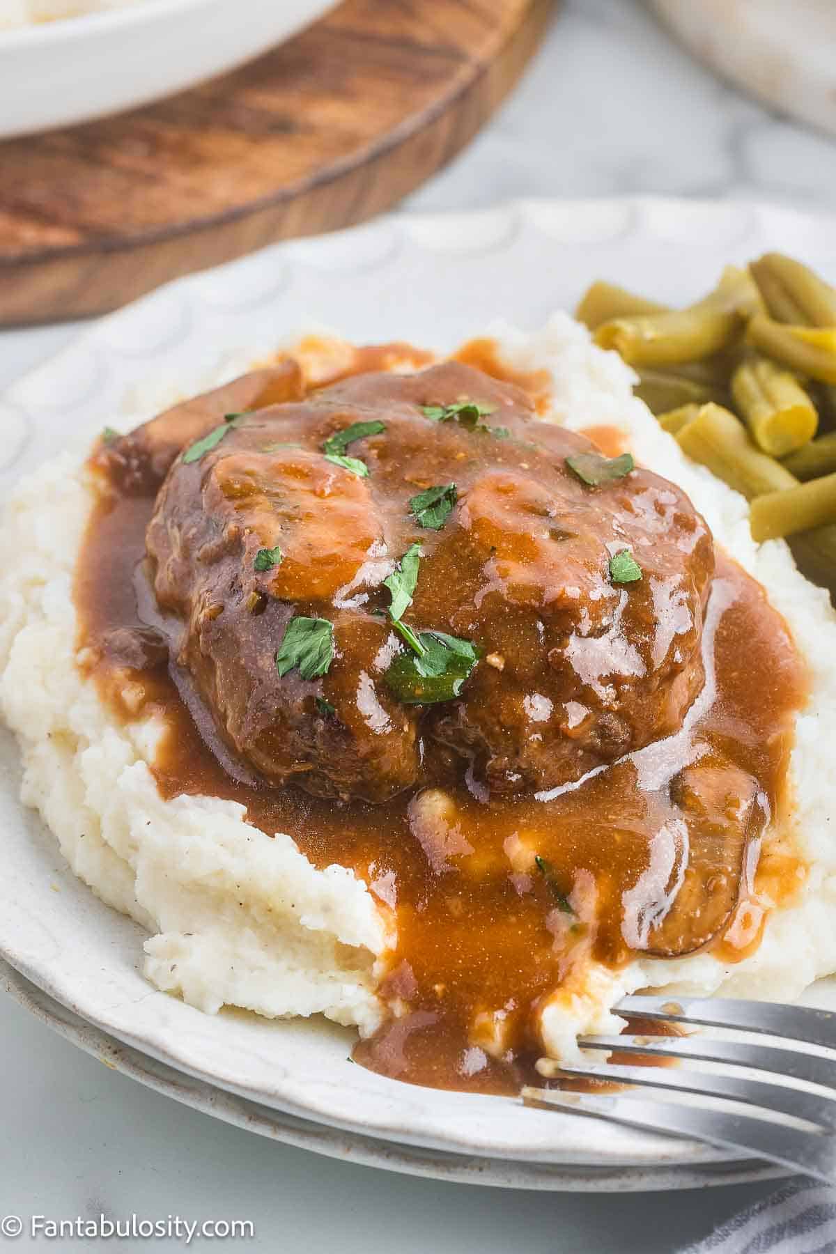 Cooked salisbury steak sitting on top of mashed potatoes, covered in mushroom gravy.