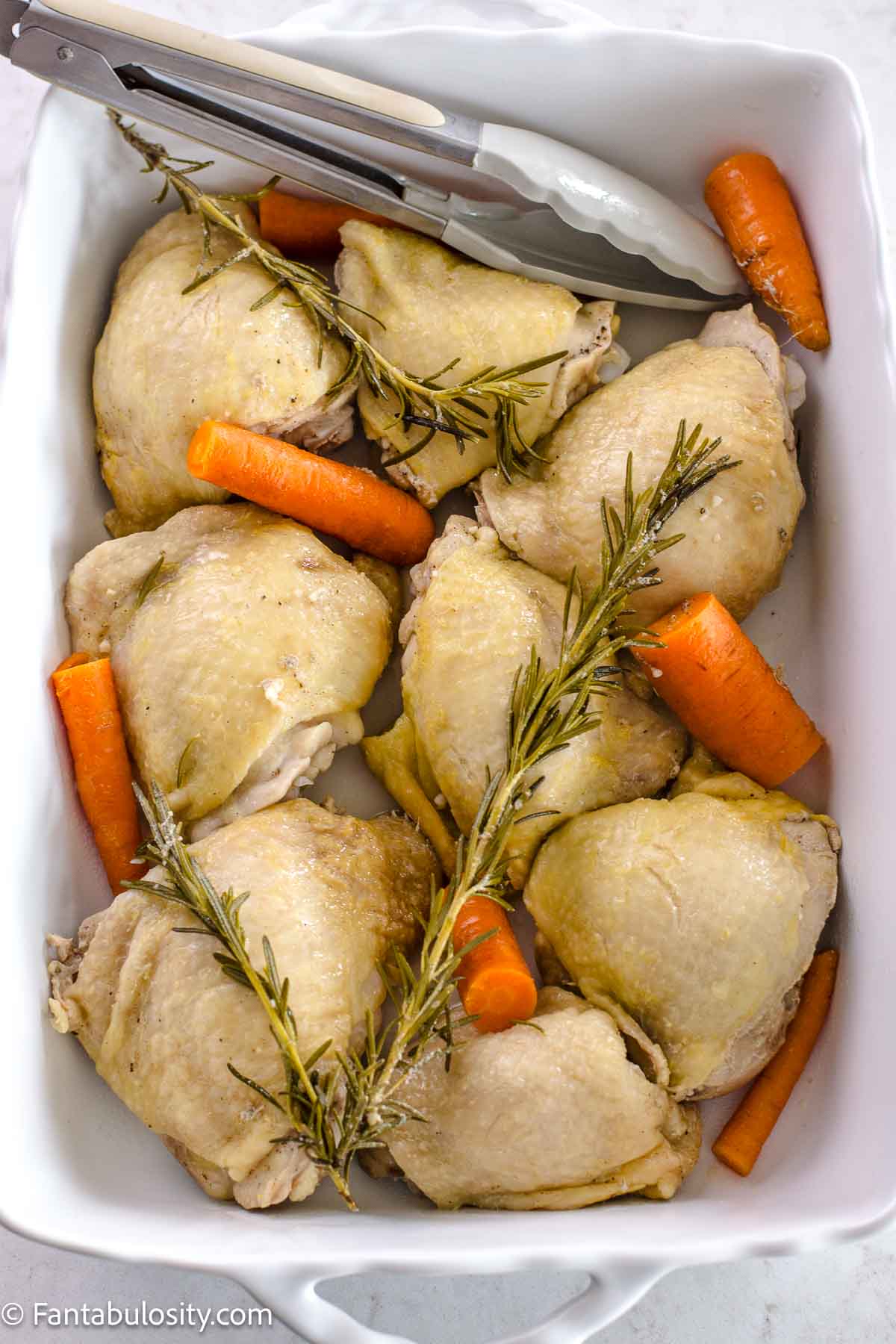 Boiled chicken thighs in baking dish, with carrots and rosemary.