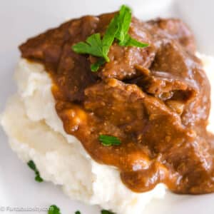 Close up of slow cooker steak on a pile of mashed potatoes.