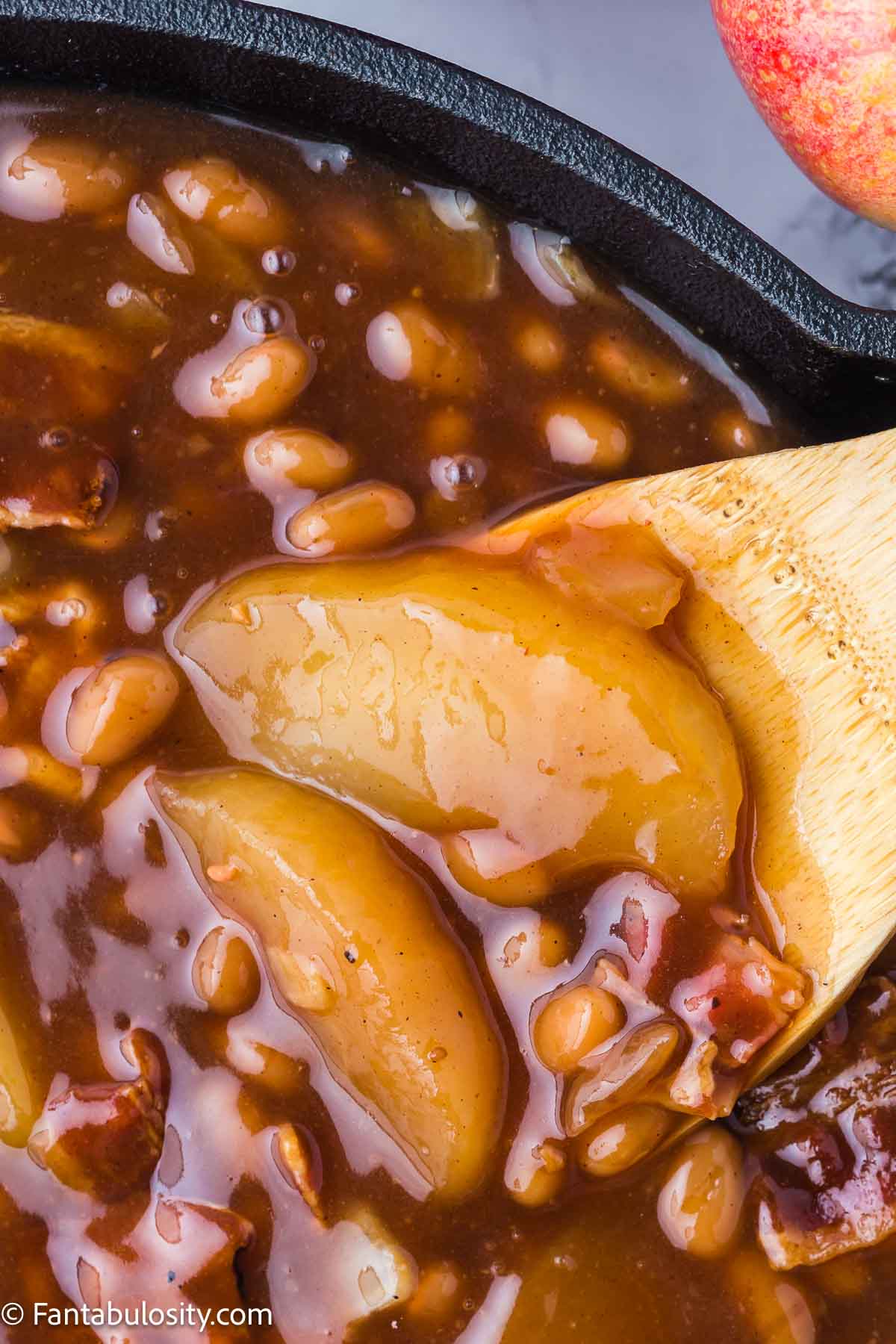 Close up of apple slices in baked beans in skillet.