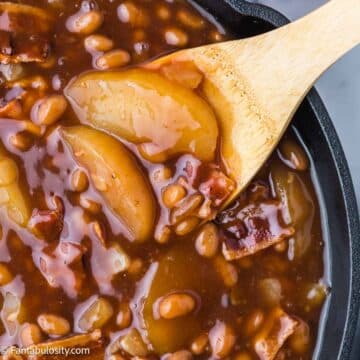 Close up of apple pie baked beans in skillet, with wooden spoon.