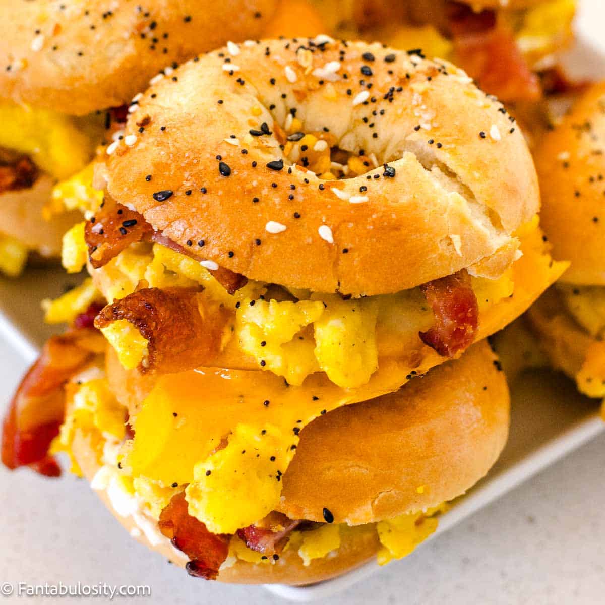Mini bagel breakfast sliders stacked on top of one another on a white plate.
