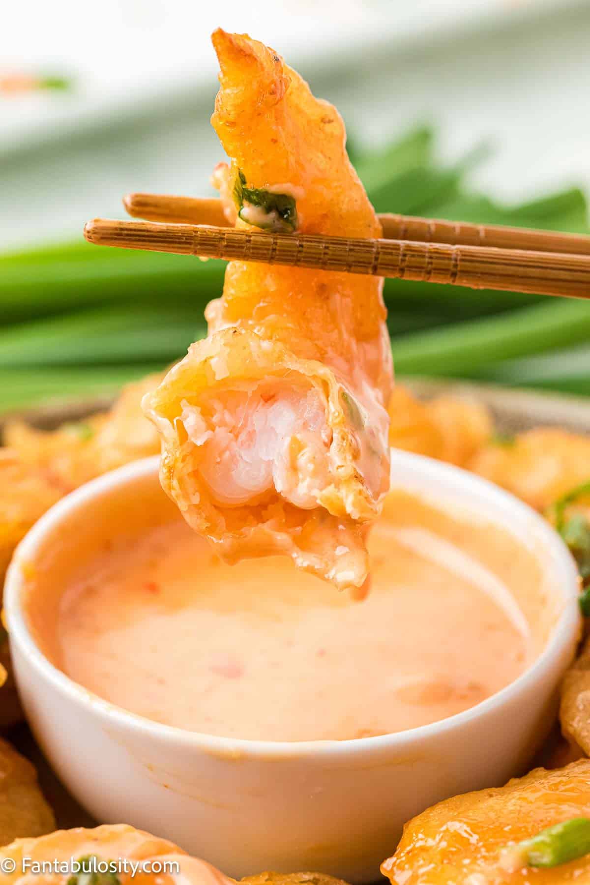Boom boom shrimp with a bite taken out of it, being dipped in more sauce.
