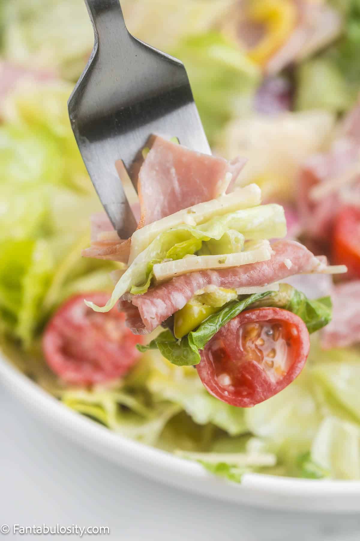 Bite of grinder salad on a fork, next to bowl of salad.