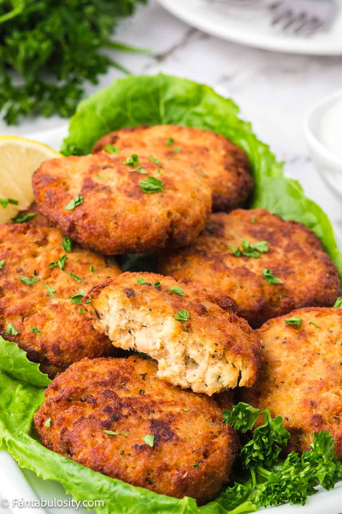 Salmon patties on plate lined with green lettuce leaves, with one patties cut open to see the inside.