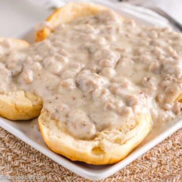 Close up of old fashioned sausage gravy poured across biscuits, sitting on a white plate.
