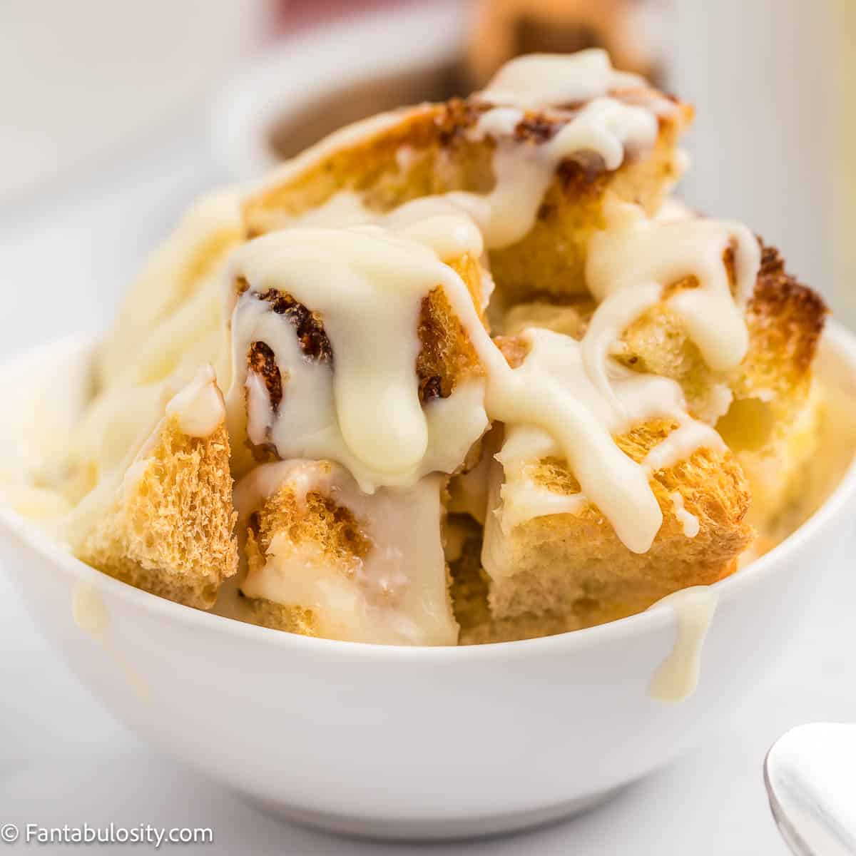 Vanilla sauce drizzled on to bread pudding, in a small white dish.
