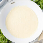 Easy Alfredo Sauce in skillet, next to fresh herbs and parmesan cheese wedge.
