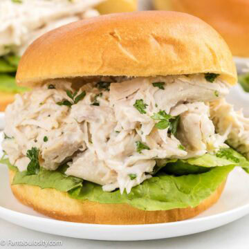 Chicken Caesar Sandwich with bun and lettuce leaf, sitting on round plate.