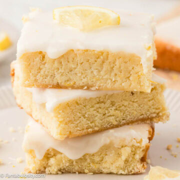 Three lemon blondies stacked on top of one another on a piece of parchment paper.